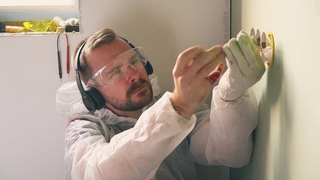 CU, Dolly cam shot: unskilled constructor in modern headphones repairs plug and passes out getting electric shock in room