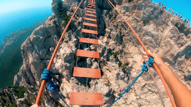 A man with a feeling of fear is walking on a rope bridge in the mountains, holding tightly to the ropes.Travel in the mountains.Adrenaline