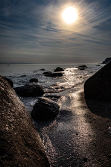 Sand Strand am Meer mit Felsen mit leichtem Wellengang in der aufgehenden Sonne bei Gegenlicht 