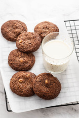 Chocolate cookies on a wire rack with milk on a white background.