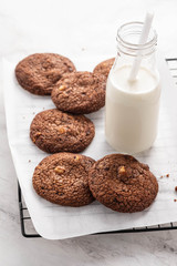 Chocolate cookies on a wire rack with milk on a white background.