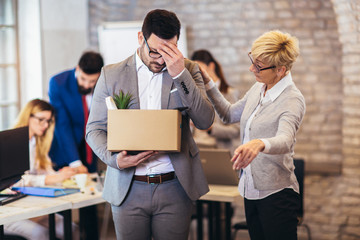 Handsome businessman in light modern office with carton box. Junior office worker gets fired by senior female manager. Last day at work.