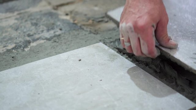 Closeup footage of tiler hand laying down tiles on the industrial glue. Tiler laying down tiles on the floor.