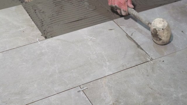 A close look at the construction tiler worker laying down the tile on cemented floor. Professional worker laying tiles on floor at construction site close-up slow motion.
