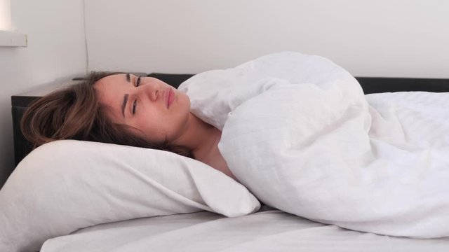 Sleepy brunette woman waking up in bed in the morning and does not want to get out of bed. not a good morning. 4k