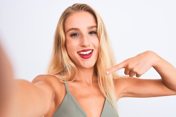 Young beautiful woman wearing t-shirt make selfie by camera over isolated white background very happy pointing with hand and finger