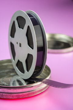old 16mm film in an aluminum bobbin and a metal box are on a pink background.
