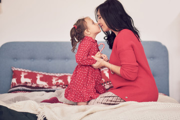 mom and daughter have fun together. a woman in a warm red knitted sweater hugs her little daughter in a red dress. family values