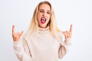 Young beautiful woman wearing turtleneck sweater standing over isolated white background shouting with crazy expression doing rock symbol with hands up. Music star. Heavy concept.
