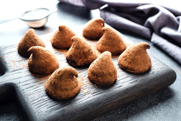Delicious chocolate truffles sprinkled with cocoa powder and walnuts on a wooden stand. Dark concrete background.
