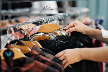 Close-up of the hands of a woman choosing clothes on a hanger in a store.