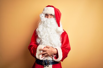 Middle age handsome man wearing Santa costume standing over isolated yellow background happy face smiling with crossed arms looking at the camera. Positive person.