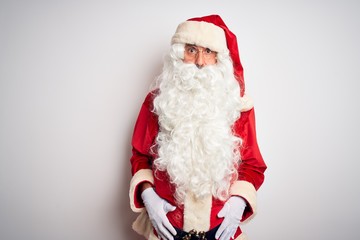 Middle age handsome man wearing Santa costume standing over isolated white background In shock face, looking skeptical and sarcastic, surprised with open mouth