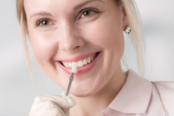 Close up of dentist using shade guide at woman's mouth to check veneer of teeth for bleaching