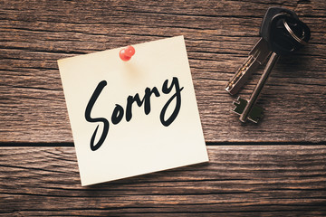 Note with the word "sorry" pinned with a thumbtack and lock keys on a wooden background: concept of regret for failure or broken relationship