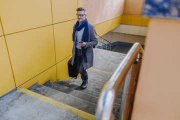 Stylish man holding cellphone and walking up the stairs