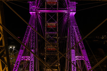 Two empty cars behind several steel wires on a giant ferris wheel covered in purple light