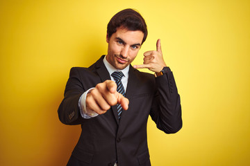 Young handsome businessman wearing suit and tie standing over isolated yellow background smiling...