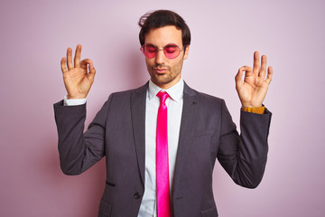 Young handsome businessman wearing suit and sunglasses over isolated pink background relax and smiling with eyes closed doing meditation gesture with fingers. Yoga concept.