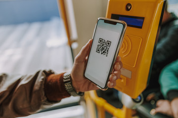 Man using smartphone and QR code to pay tram fare