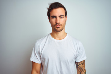 Young handsome man with tattoo wearing casual t-shirt over isolated white background with serious expression on face. Simple and natural looking at the camera.