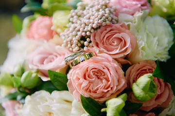 Close up of two golden wedding rings on bridal bouquet of pink and white roses outdoors, copy space. Selective focuse. Wedding concept
