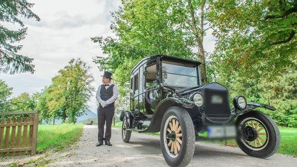 A chauffeur standing by the side of black vintage car and waiting for the owner. Slovenia. Low angle.