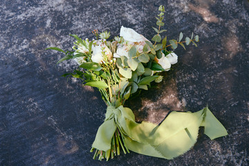 Top view of bridal bouquet of white roses and green ribbon on stone background outdoors, copy space. Wedding concept