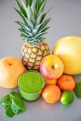 Different tropical fruits and green smoothie on grey background, healthy eating lifestyle concept