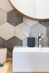 Interior of a house private bathroom. hexagonal Tiles with natural colors on gray brown in a bathroom interior furnishings and supplies majolica laid on the wall near a sink with toothbrush and mirror