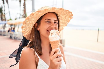 Young beautiful woman eating ice cream cone by the beach on a sunny day of summer on holidays