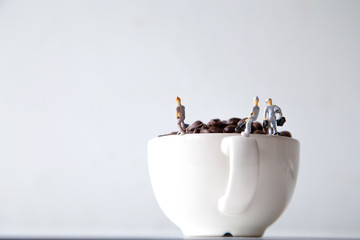 miniature people standing on a white coffee cup with brown coffee beans, Concept: teamwork professionalism and beverage business ideas successful, close-up macro toy small creative lifestyle