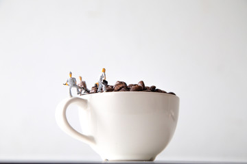 miniature people standing on a white coffee cup with brown coffee beans, Concept: teamwork...