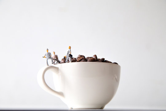 miniature people standing on a white coffee cup with brown coffee beans, Concept: teamwork professionalism and beverage business ideas successful, close-up macro toy small creative lifestyle