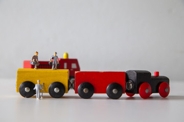 Obraz na płótnie Canvas Miniature people car works on a multicolored Wooden car on a white wooden table, Creative background Teamwork for global transportation, Concept: Education for children learning in school