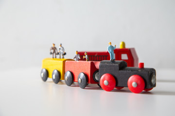 Fototapeta premium Miniature people car works on a multicolored Wooden car on a white wooden table,&nbsp;Creative background Teamwork for global transportation, Concept: Education for children learning in school