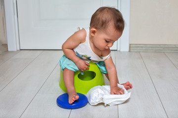 potty training concept. A cute little baby sits on a green pot and plays with a diaper in the room. close-up, soft focus, place for copy space