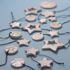 Fototapeta na wymiar Small ornament pendant star shape, snowflake round figures from white clay and shining glitter. Shallow depth of focus, bokeh effect on blue background. Christmas and New year decoration, jewel gift.