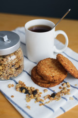 Fototapeta na wymiar round brown wholemeal oatmeal cookies stack with granola and black coffee in white cup on striped textile napkin on wooden table, close up side view of vertical still life stock photo image