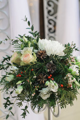 bridal flower composition with chrysanthemum, rose, pine branch and cone, eustoma, ilex, thuja, waxflover, Eucalyptus parvifolia on high stand on floor for winter wedding, closeup vertical photo image