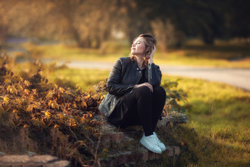 Naklejka na ściany i meble Girl sitting in the sunlight in autumn in the Park