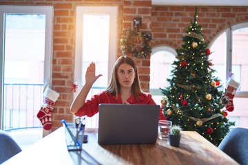 Beautiful woman sitting at the table working with laptop at home around christmas tree Swearing...