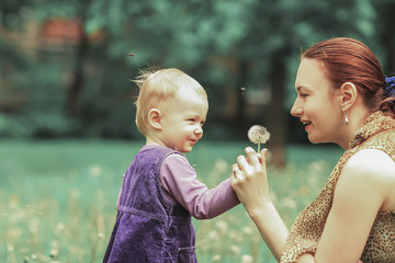 young mother teaches her little daughter to blow on a dandelion