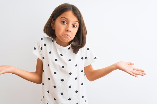 Young beautiful child girl wearing casual t-shirt standing over isolated white background clueless and confused expression with arms and hands raised. Doubt concept.