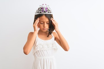 Beautiful child girl wearing princess crown standing over isolated white background with hand on head for pain in head because stress. Suffering migraine.