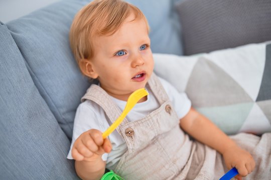 Adorable blonde toddler sitting on the sofa playing with plastic meals toys at kindergarten