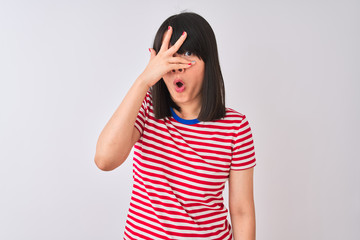 Young beautiful chinese woman wearing red striped t-shirt over isolated white background peeking in shock covering face and eyes with hand, looking through fingers with embarrassed expression.