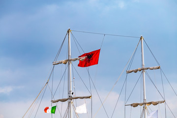 Mast of vintage mast wooden sailing ship for sea tours in port of Saranda, Albania with red state albanian flag with black double-headed eagle, and italian flag.