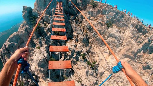 A test of courage.The boy walks with great care over a rope bridge in the mountains, holding fast to the ropes.Mountain extreme sport.