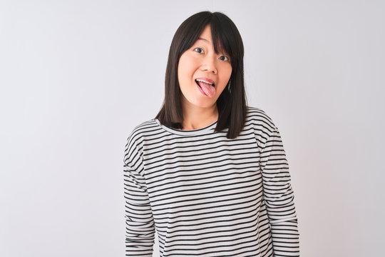 Young beautiful chinese woman wearing black striped t-shirt over isolated white background sticking tongue out happy with funny expression. Emotion concept.